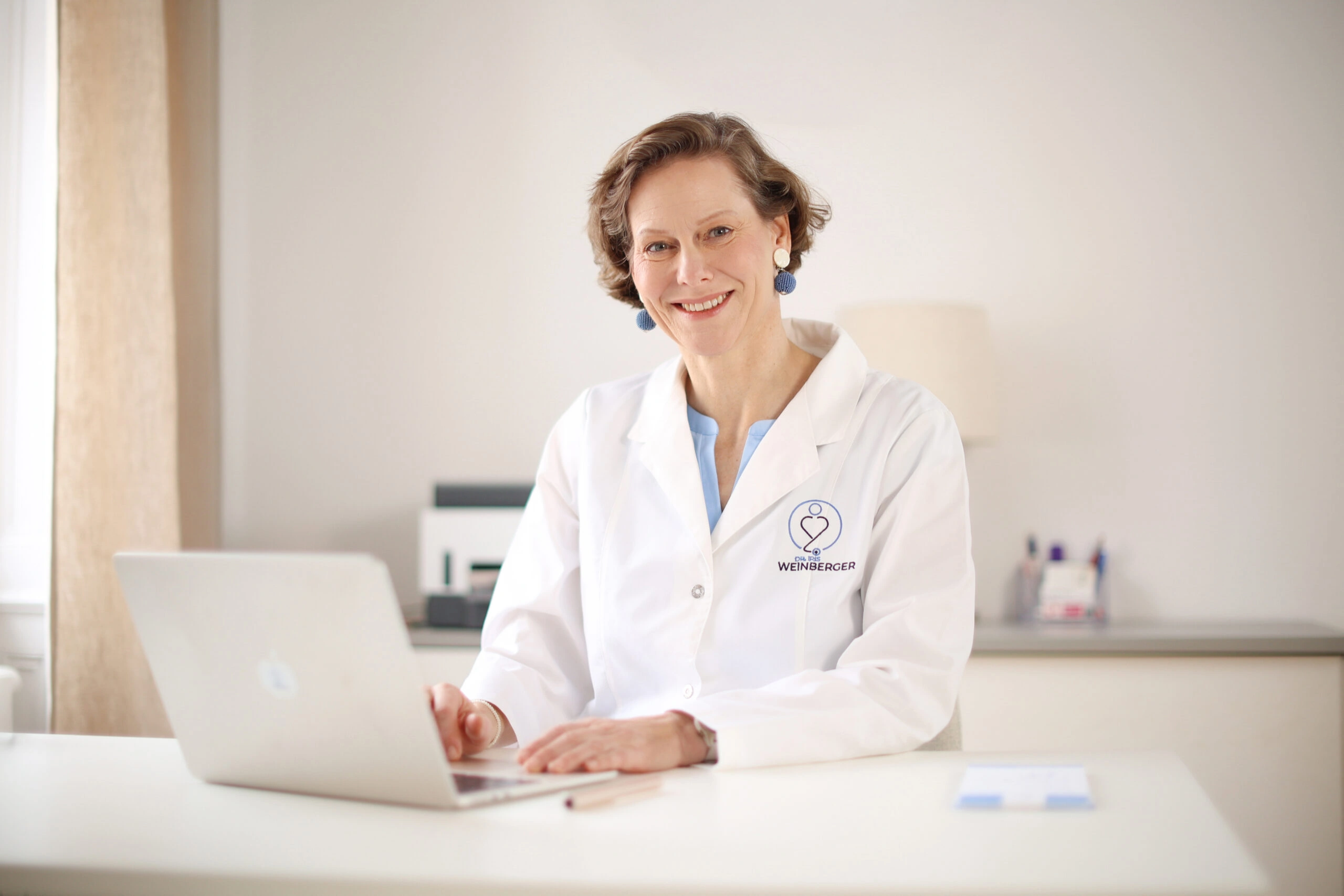 Dr. Iris Weinberger sitzt als Ärztin vor dem Laptop in ihrer Praxis